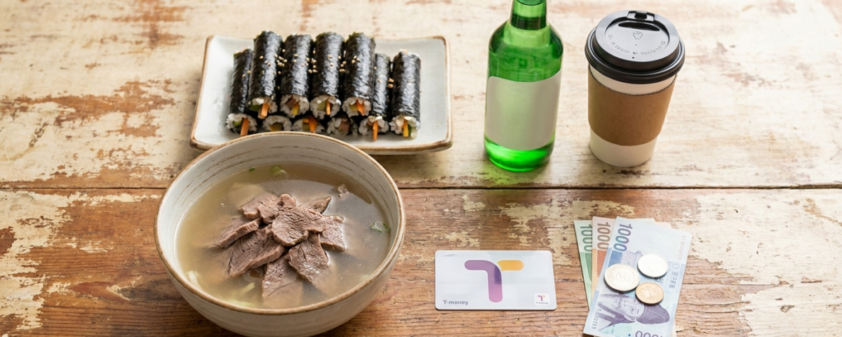 곰탕, 김밥, 커피, 소주, 교통카드와 한국 원화 지폐가 놓인 나무 탁자